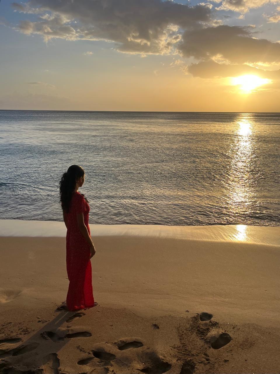Femme en robe rouge contemplant la mer au coucher du soleil, Guadeloupe